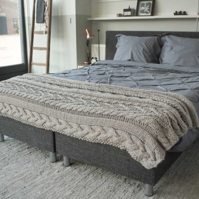slaapkamer met bed en handgebreide sprei op grijs dekbedovertrek van katoen percal