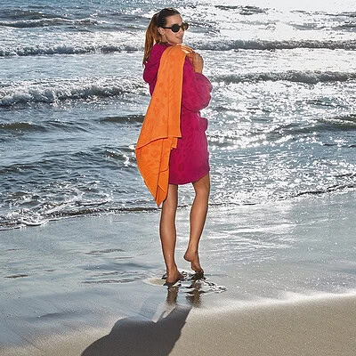 vrouw op strand in fel gekleurde dames badjas met strandlaken